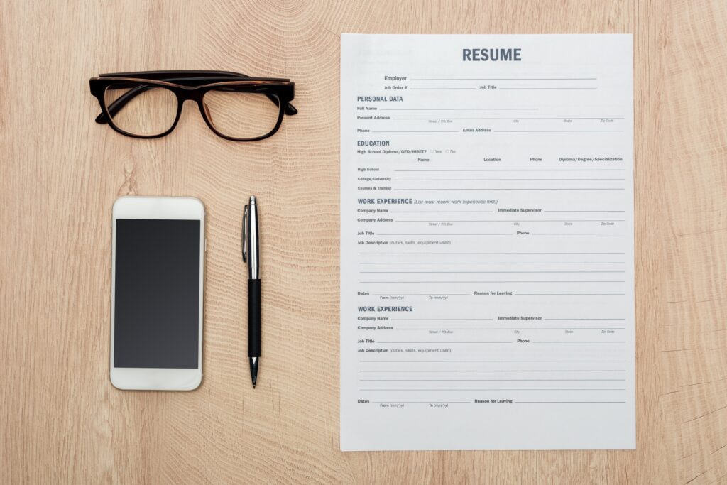 flat lay with glasses, pen, smartphone with blank screen and resume template on wooden surface