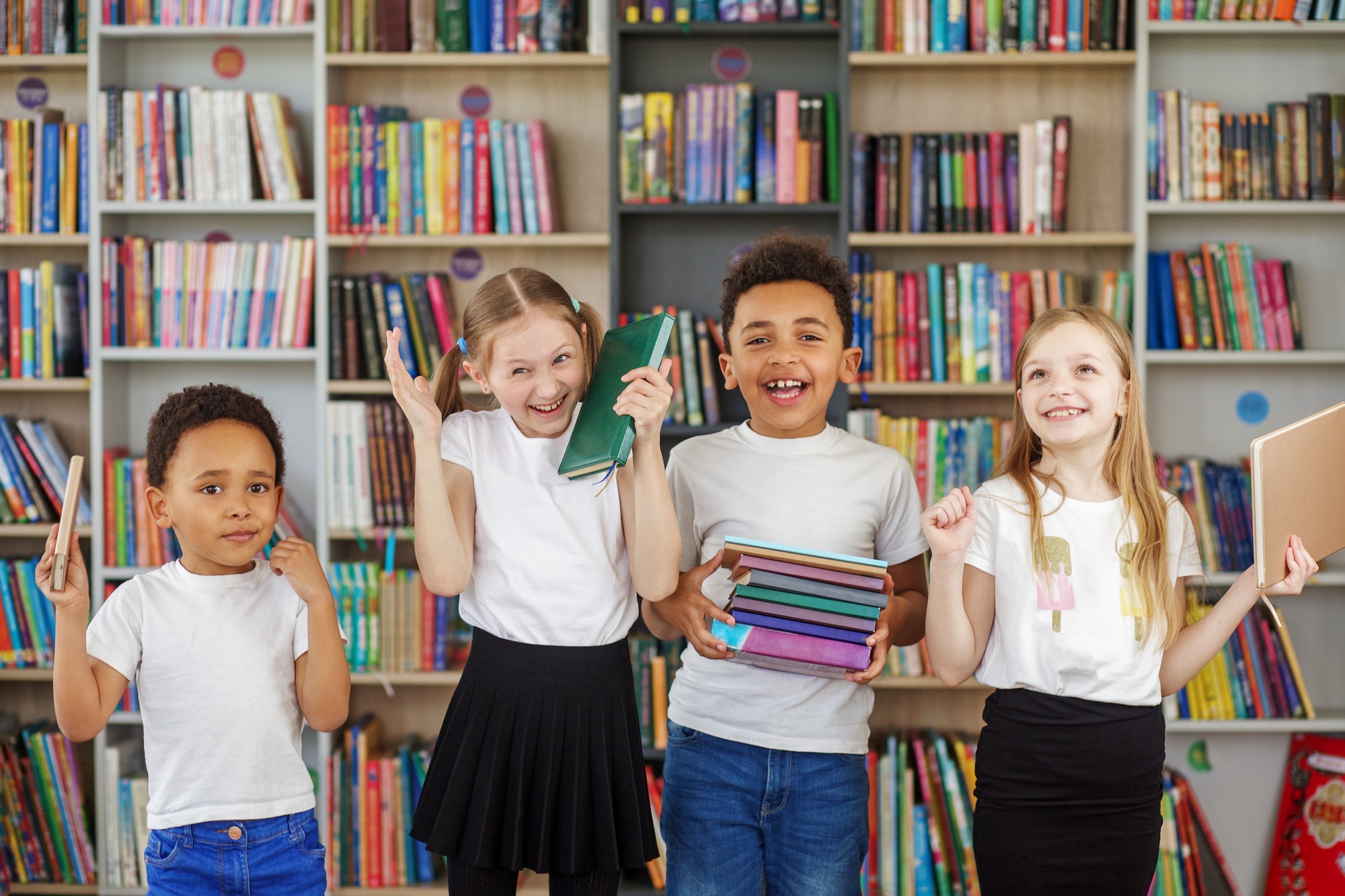 Four children holding stack of books in library. Multiethnic classmates having fun. Back to school.