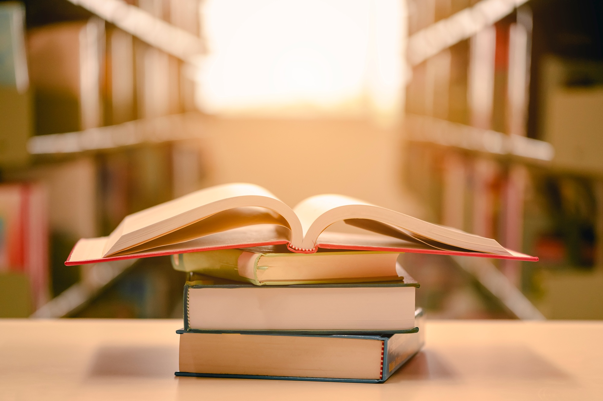 Opened book with stack of books on the desk wood in the library. Education background concept.